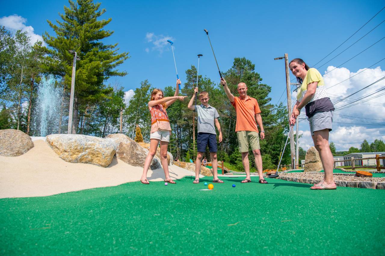 A family waves their golf clubs in the air while a woman puts a ball into a hole. 